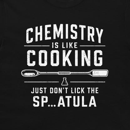 A close-up of a black t-shirt featuring a distressed white graphic print that reads 'CHEMISTRY IS LIKE COOKING JUST DON'T LICK THE SP...ATULA'.