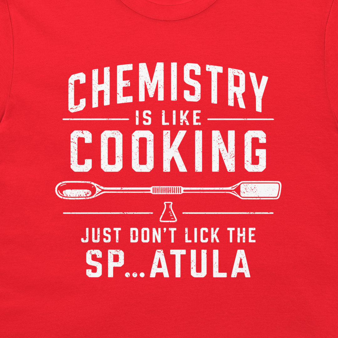 A close-up of a bright red t-shirt, featuring a distressed white graphic print that reads 'CHEMISTRY IS LIKE COOKING' and 'JUST DON'T LICK THE SP...ATULA'.