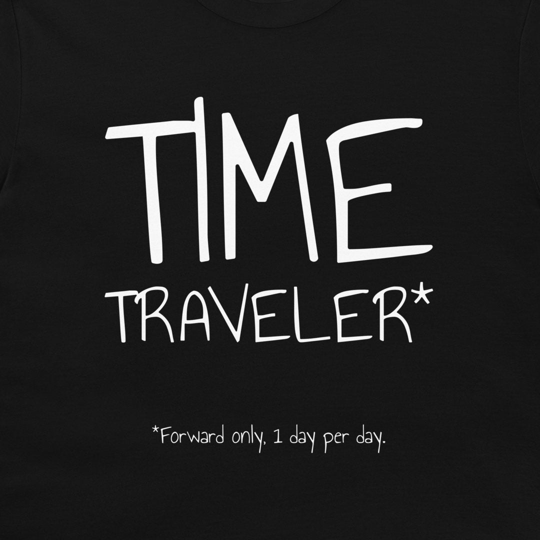 A close-up of a black t-shirt featuring a white graphic print that reads 'TIME TRAVELER*' with the note '*Forward only, 1 day per day.' printed below.