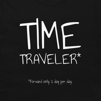 A close-up of a black t-shirt featuring a white graphic print that reads 'TIME TRAVELER*' with the note '*Forward only, 1 day per day.' printed below.