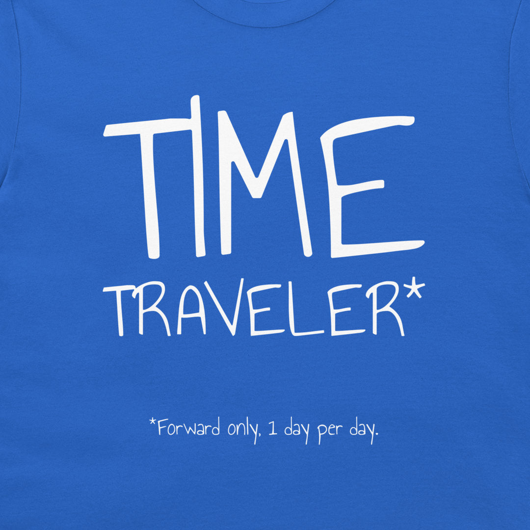 A close-up of a blue t-shirt featuring a white graphic print that reads 'TIME TRAVELER*' with the note '*Forward only, 1 day per day.' printed below.