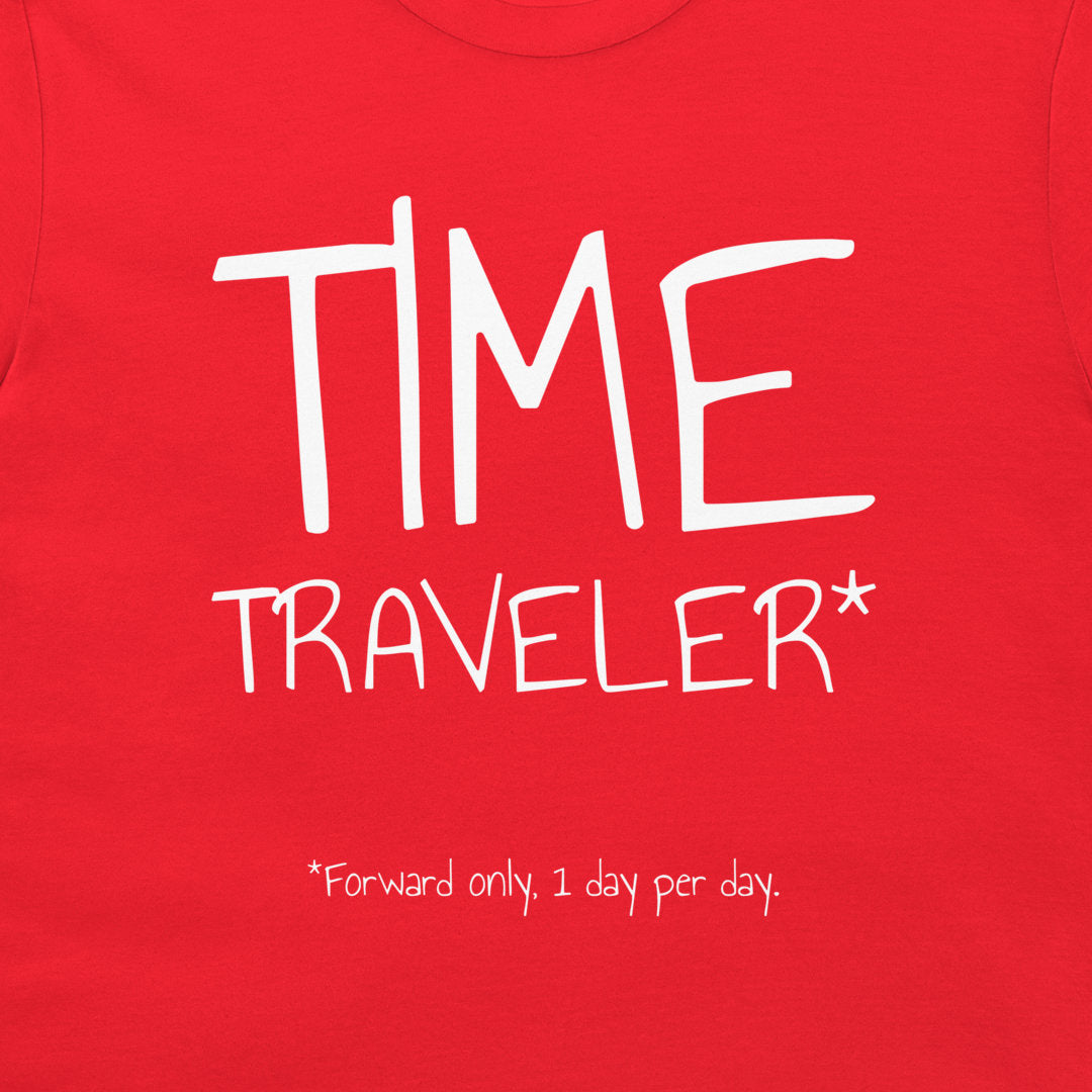 A close-up of a bright red t-shirt featuring a white graphic print that reads 'TIME TRAVELER*' with a small footnote '*Forward only, 1 day per day.' below it.