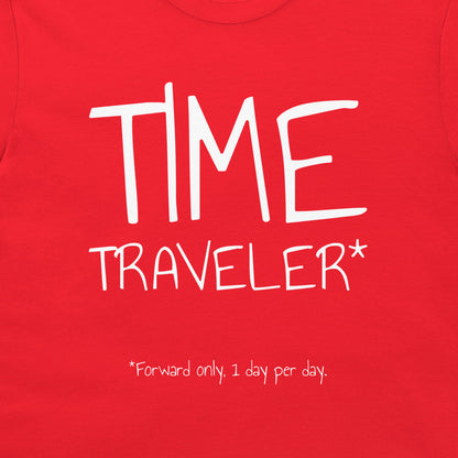 A close-up of a bright red t-shirt featuring a white graphic print that reads 'TIME TRAVELER*' with a small footnote '*Forward only, 1 day per day.' below it.