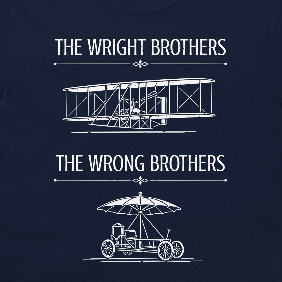 A navy blue t-shirt featuring a white graphic print with the text 'THE WRIGHT BROTHERS' above a line drawing of a vintage biplane, and 'THE WRONG BROTHERS' below a line drawing of an early automobile with an umbrella.