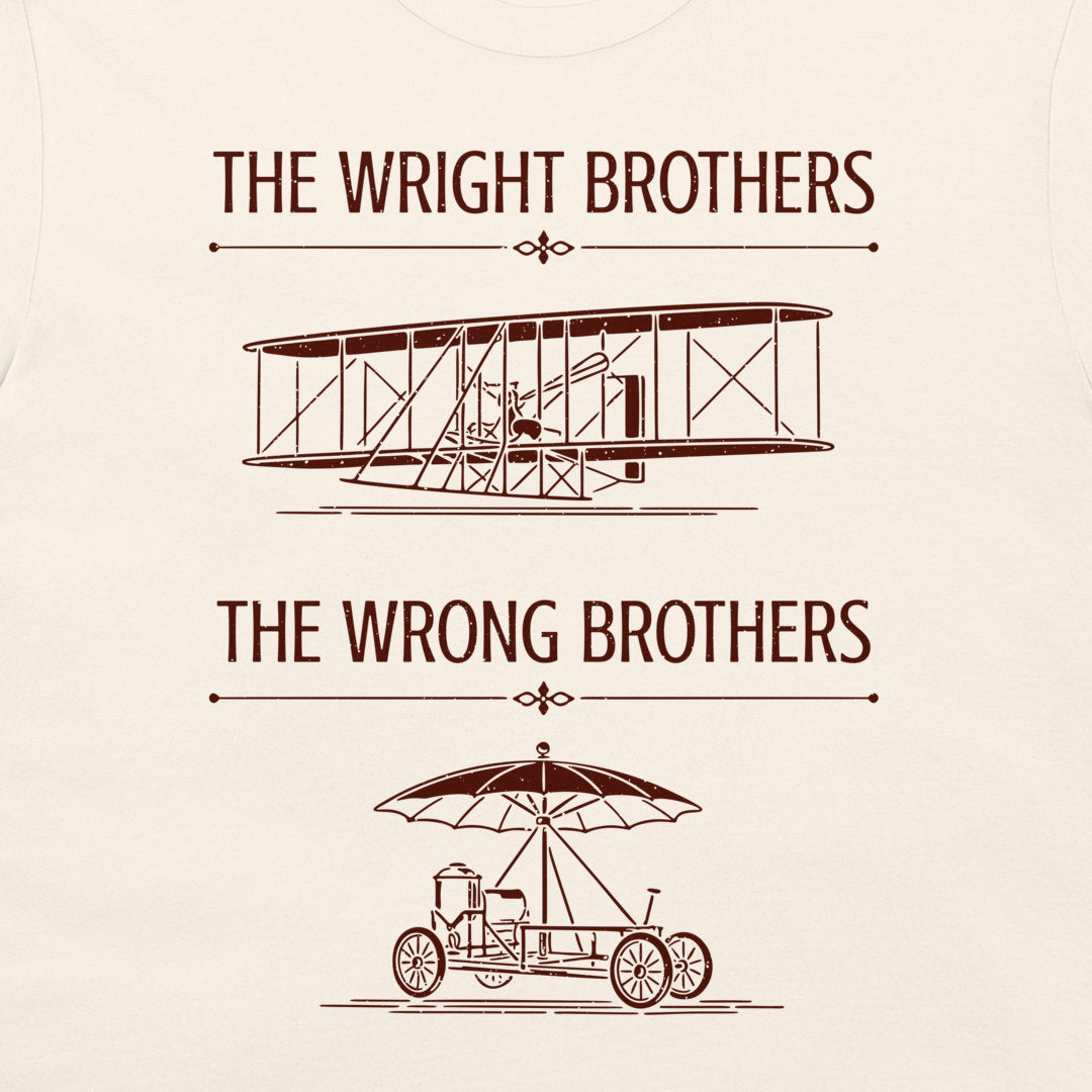 A natural t-shirt featuring a brown graphic print with the text 'THE WRIGHT BROTHERS' above a line drawing of a vintage biplane, and 'THE WRONG BROTHERS' below a line drawing of an early automobile with an umbrella.