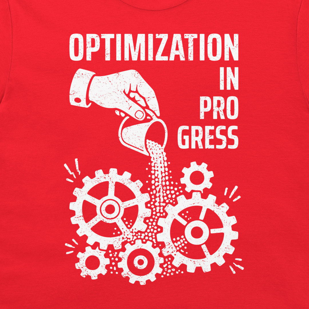 A close-up of a red garment, likely a t-shirt, featuring a white distressed graphic print that reads 'OPTIMIZATION IN PROGRESS' above a hand pouring sand into gears.