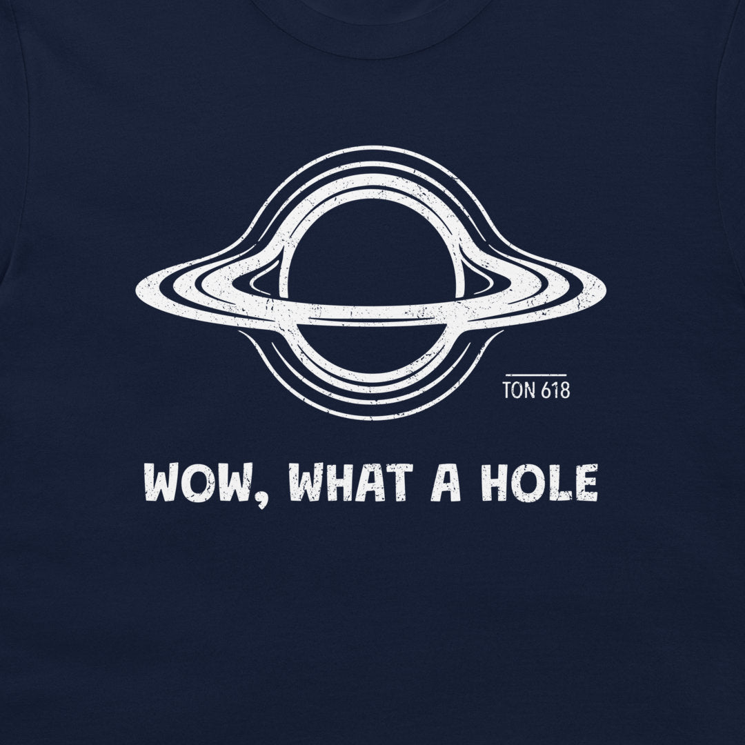 A close-up of a navy blue t-shirt, featuring a white distressed graphic o a black hole with the text 'WOW, WHAT A HOLE' and 'TON 618' printed below it.