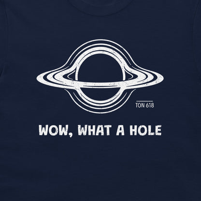 A close-up of a navy blue t-shirt, featuring a white distressed graphic o a black hole with the text 'WOW, WHAT A HOLE' and 'TON 618' printed below it.