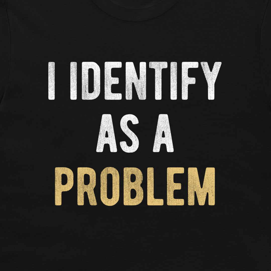 A close-up of a black t-shirt, featuring the text 'I IDENTIFY AS A PROBLEM' printed on the chest. 