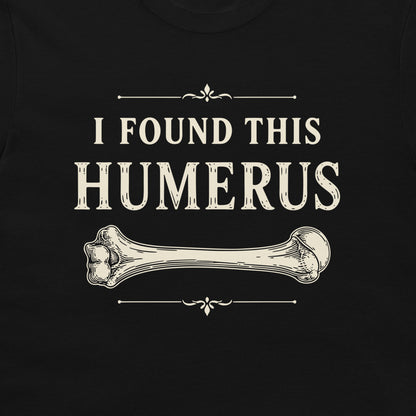 A close-up of a black garment featuring a distressed cream-colored graphic print that reads 'I FOUND THIS HUMERUS' above and below a detailed illustration of a bone.