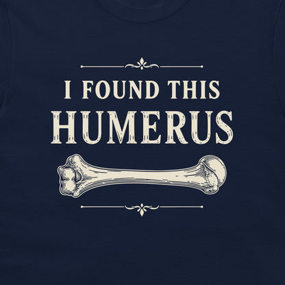 A close-up of a navy blue garment, likely a t-shirt, featuring a vintage-style cream graphic that reads 'I FOUND THIS HUMERUS' above an illustration of a bone.