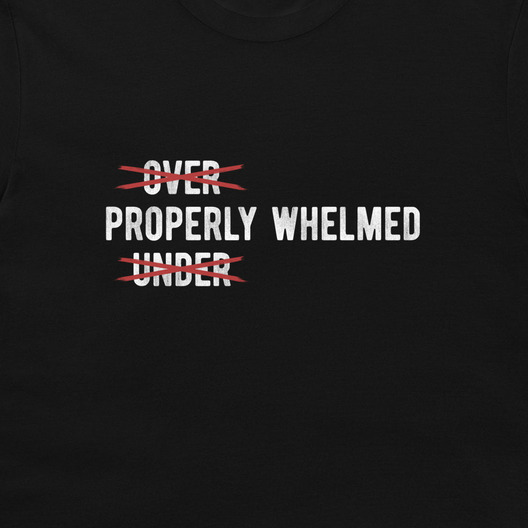 A close-up of a black t-shirt featuring a graphic print with the words 'OVER PROPERLY WHELMED' and 'UNDER' crossed out in red scribbles.