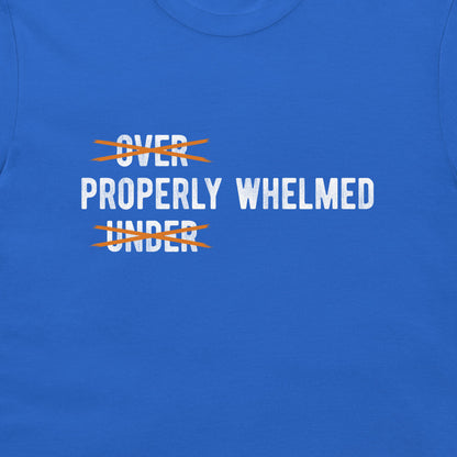 A close-up of a royal blue t-shirt featuring a graphic print. The text reads 'PROPERLY WHELMED' in white capital letters, with 'OVER' and 'UNDER' crossed out in orange scribbles.