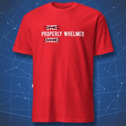 A red short-sleeve crewneck t-shirt with a white graphic text print reading 'OVER PROPERLY WHELMED' crossed out with black lines, displayed against a blue starry background.