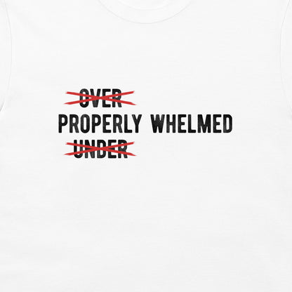 White t-shirt featuring a graphic print with the words 'OVER' and 'UNDER' in black text, both crossed out with red scribbles, leaving 'PROPERLY WHELMED' printed in the center.